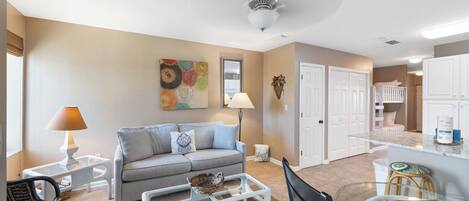A living room with a sofa, coffee table, and chairs, a dining area with a table and chairs, and a kitchen with cabinets and a countertop.