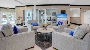 Un hall d’entrée avec des canapés gris, une table ronde et un écran de télévision.