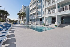 Un espace piscine comprenant des chaises longues, une piscine et un immeuble à plusieurs étages doté de balcons.