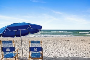 A beach with two blue beach chairs and a blue umbrella.