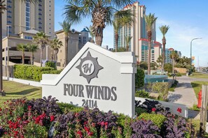 A sign for 'Four Winds 2414' with a star logo, surrounded by greenery and palm trees.