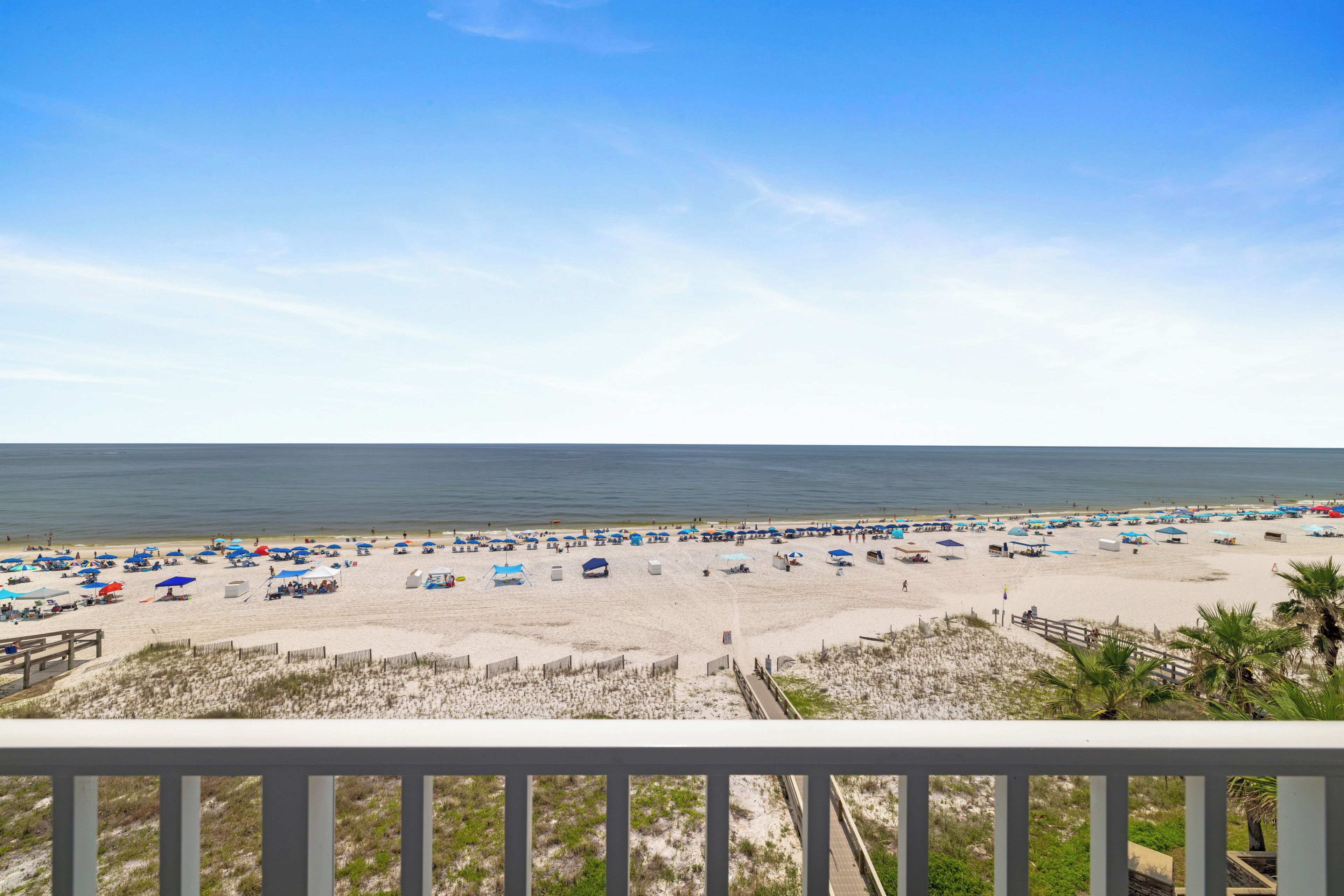 A beach with numerous umbrellas and sun loungers, a wooden walkway, and a clear view of the ocean.