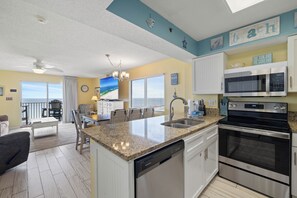 A modern kitchen with granite countertops, stainless steel appliances, and a view to the outside. - Four Winds 604 by Liquid Life (Orange Beach)