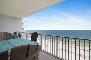 A balcony with a view of the beach, a table, chairs, and a striped chair. - Lighthouse 1206 by Liquid Life (Gulf Shores)