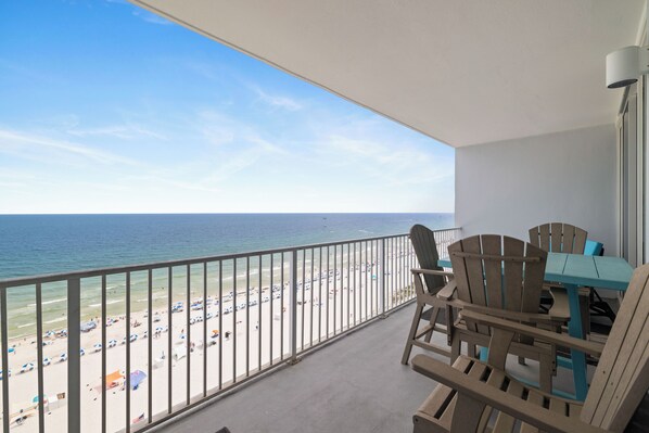 A balcony with a view of the beach, wooden chairs, a table, and a railing. - Lighthouse 1206 by Liquid Life (Gulf Shores)