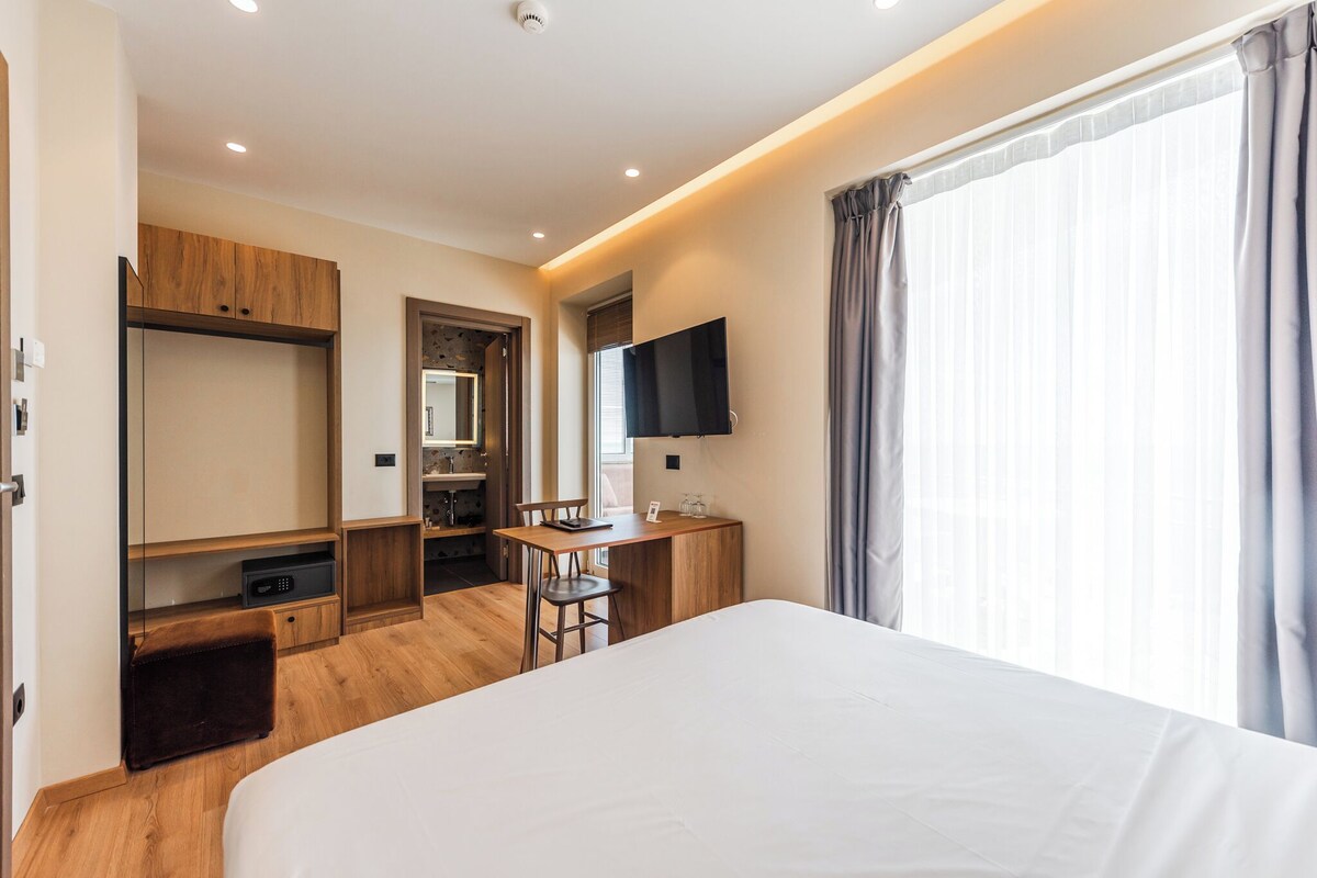 Una habitación de hotel moderna con una cama grande, un escritorio con silla, un televisor y un armario.