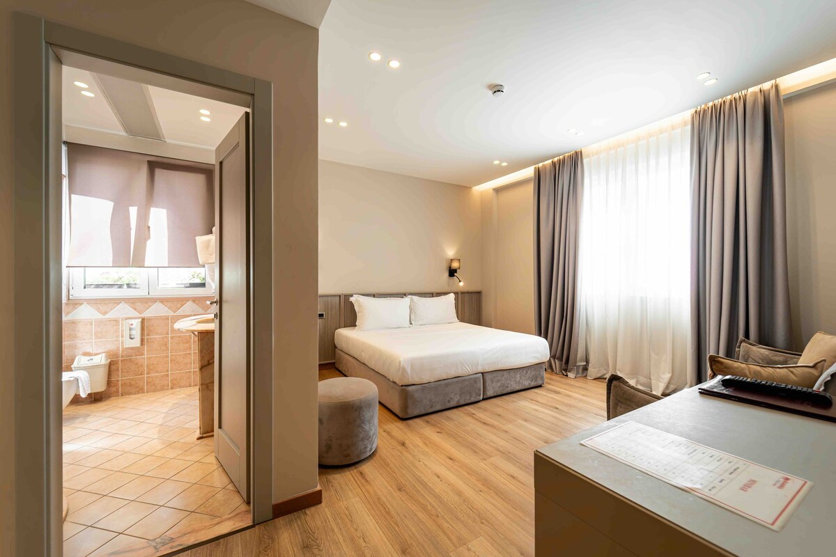 A hotel room with a bed, a desk, a chair, a bathroom, and a view of the outdoors.