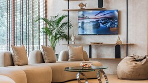A modern living room with a sofa, a glass coffee table, a TV mounted on the wall, and a potted plant. - Aragosta Hotel (Durrës)