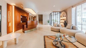 A modern hotel lobby with a reception desk, seating area, and large windows. - Aragosta Hotel (Durrës)