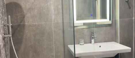 A modern bathroom with a glass-enclosed shower, a white sink, and a mirror above it.