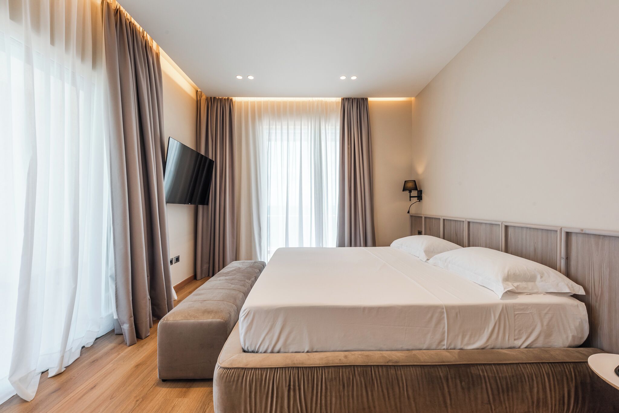 A modern hotel room with a large bed, a flat-screen TV, and a bench.