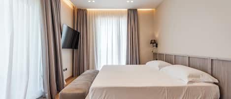 A modern hotel room with a large bed, a flat-screen TV, and a bench.