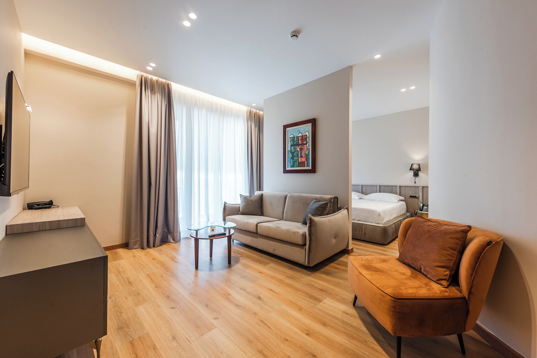 A modern hotel room with a sofa, a bed, a small table, and a desk.