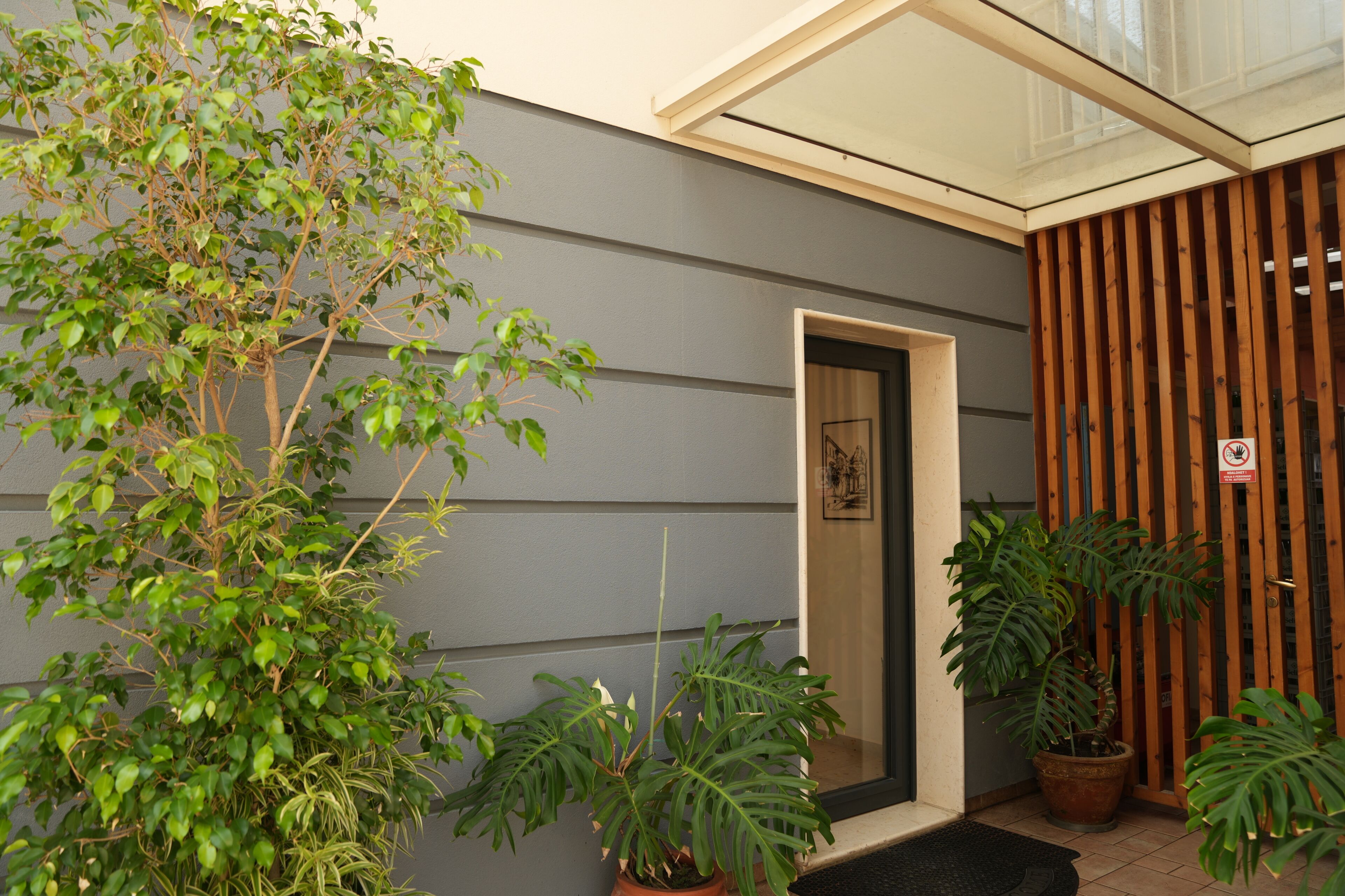 A modern building exterior with a grey siding, a wooden door, and a glass entrance.