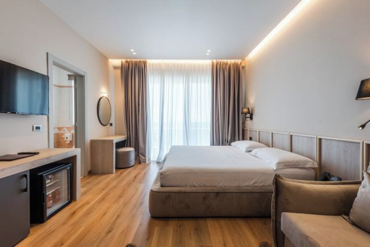 A modern hotel room with a bed, a desk, a chair, a television, and a mirror.