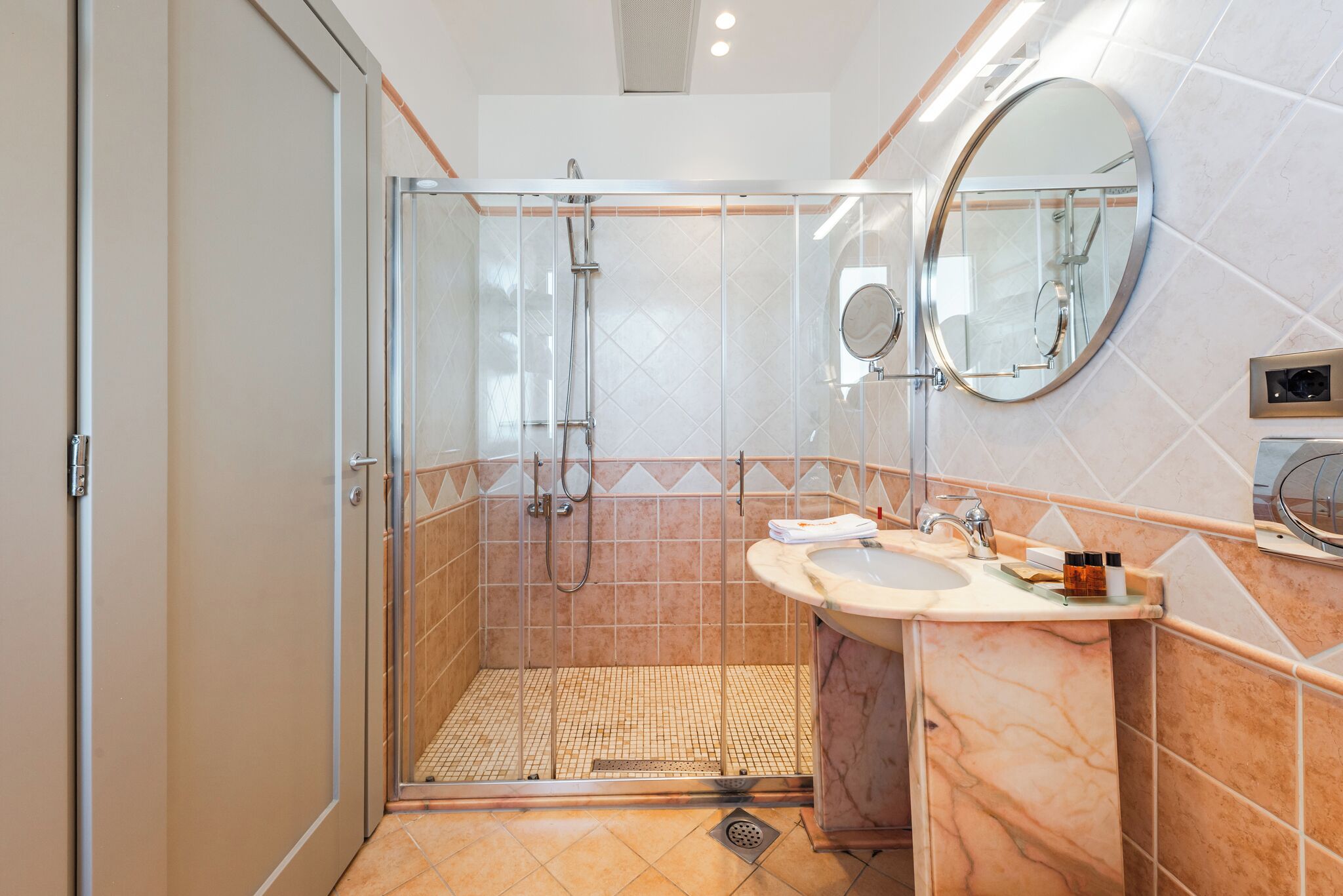 A modern bathroom with a glass-enclosed shower, a sink with a marble countertop, and a large mirror.