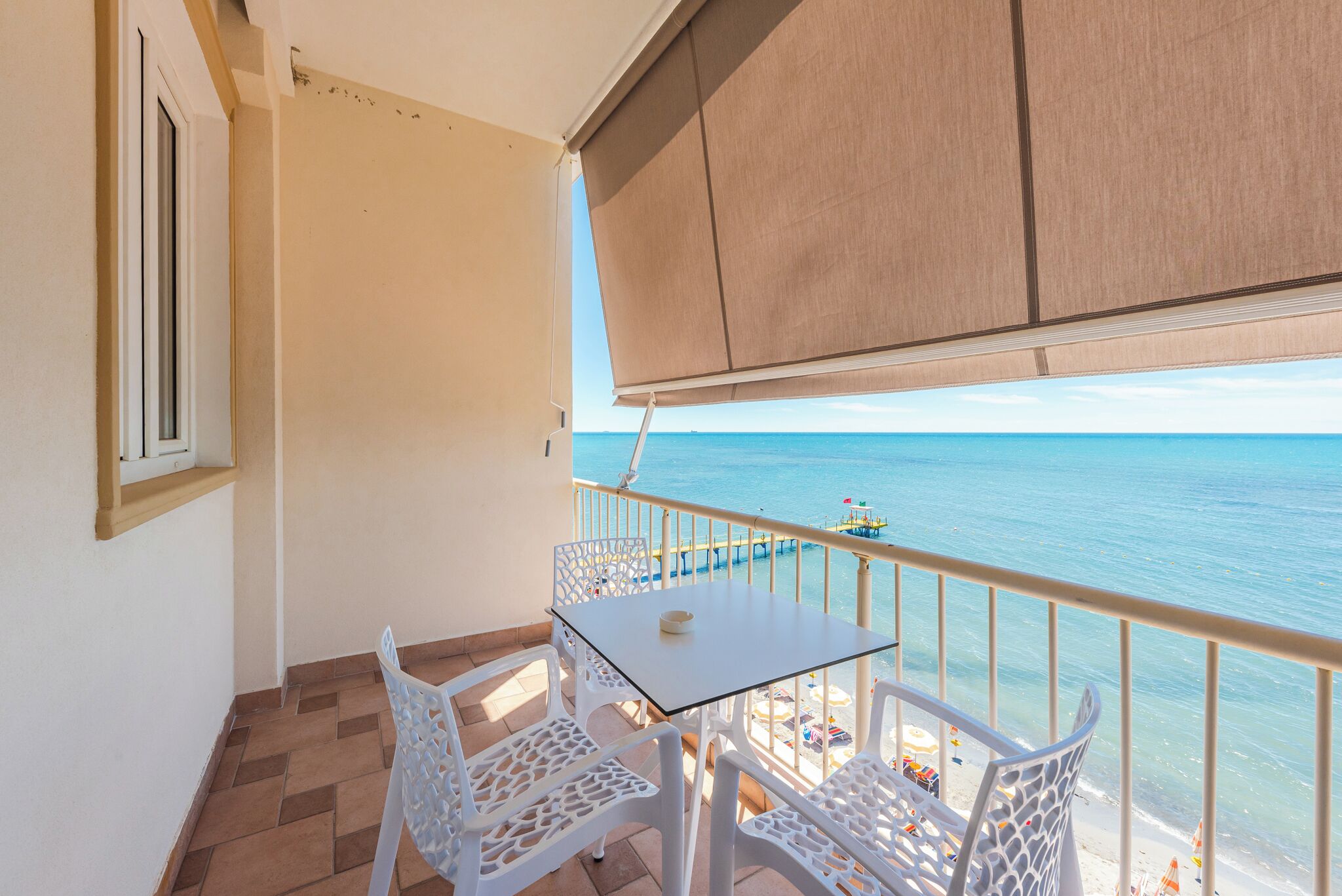 A balcony with a table and chairs, overlooking a beach and the sea.