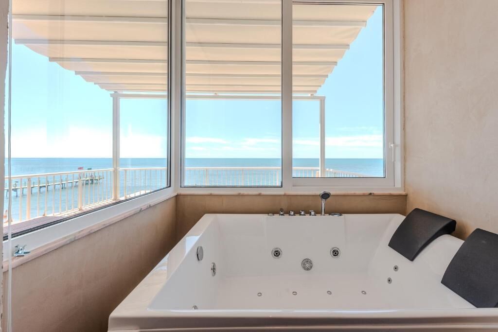 A large, empty bathtub with a view of the sea through a large window.