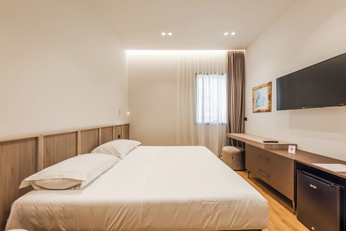 Una habitación de hotel moderna con una cama grande, un escritorio con televisor de pantalla plana y un minibar.