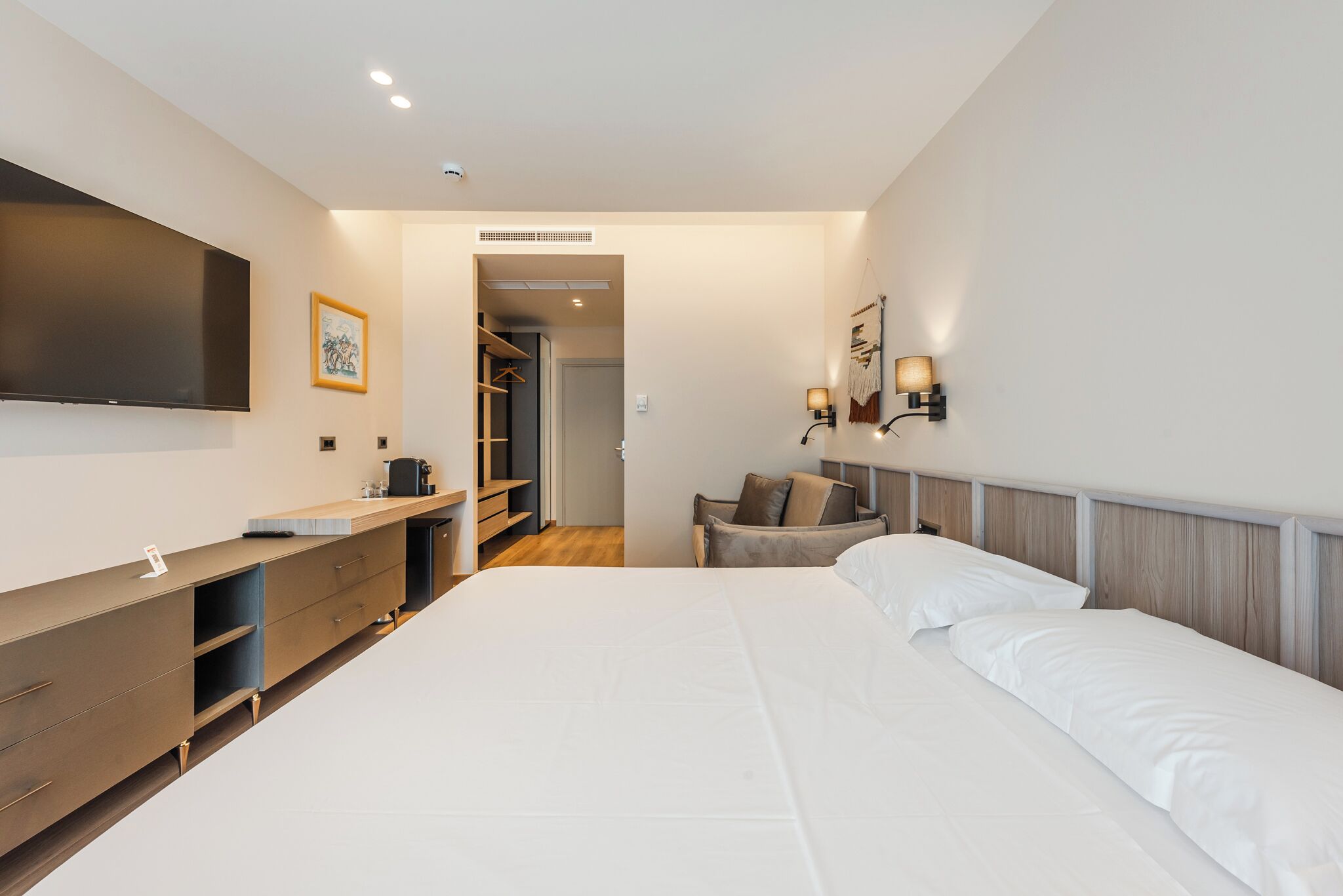 Une chambre d’hôtel moderne dotée d’un grand lit, d’un bureau avec des tiroirs, d’une télévision à écran plat et d’une armoire.