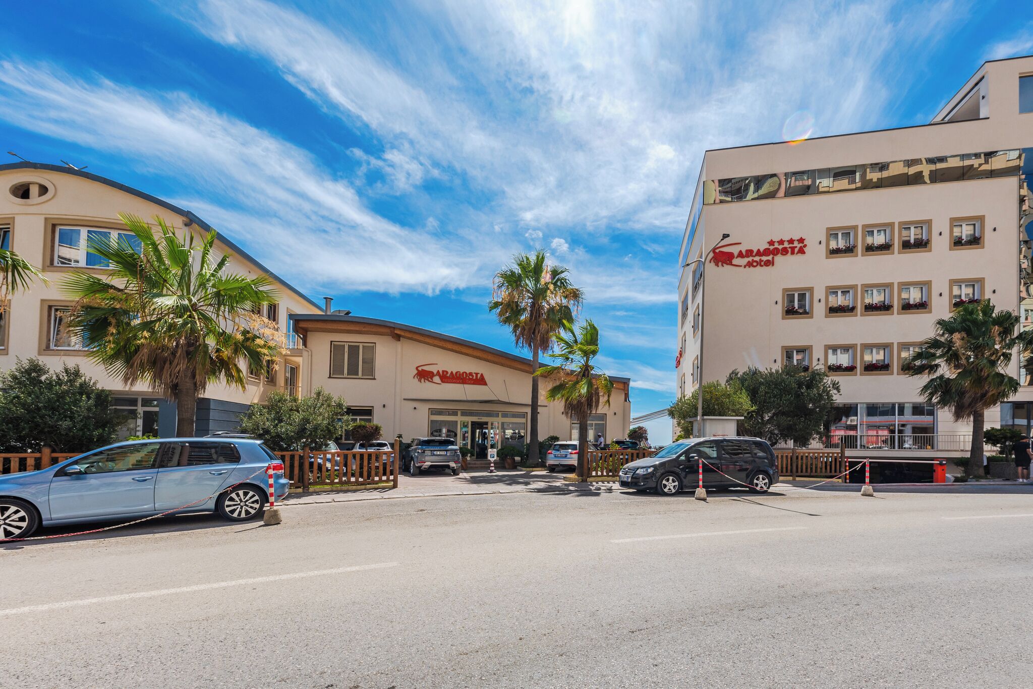 A hotel with a modern facade, palm trees, and a clear blue sky.