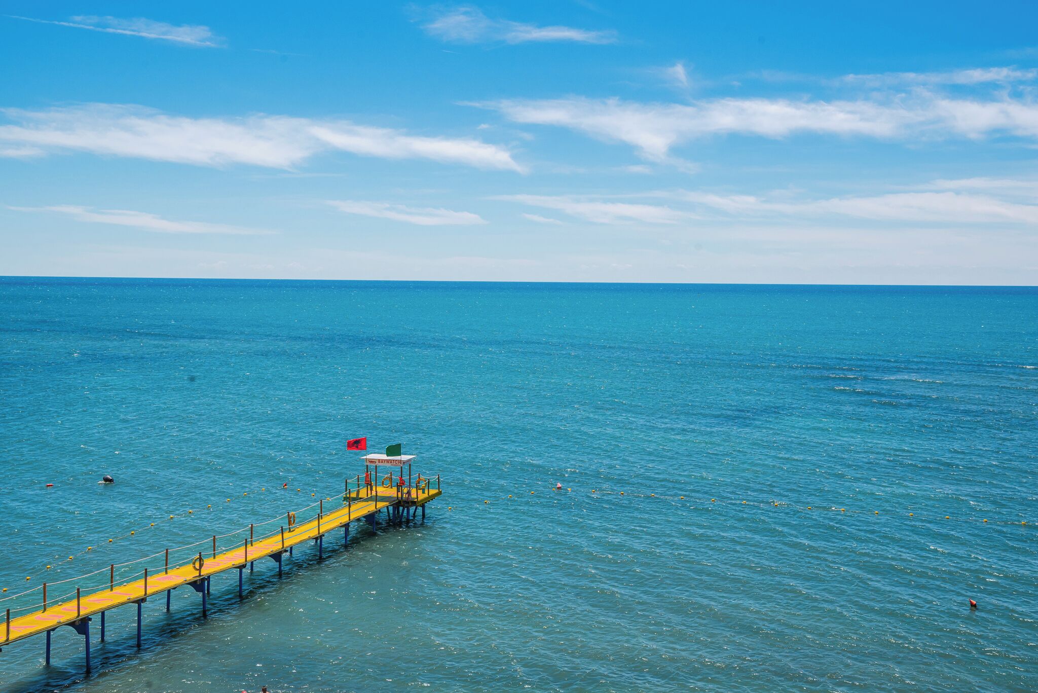 A pier extending into a calm sea with clear skies.