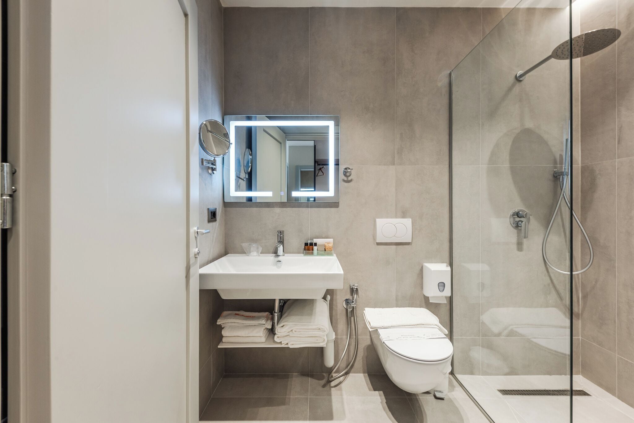 Une salle de bain moderne avec une douche à parois de verre, un lavabo blanc avec un miroir au-dessus et des toilettes.