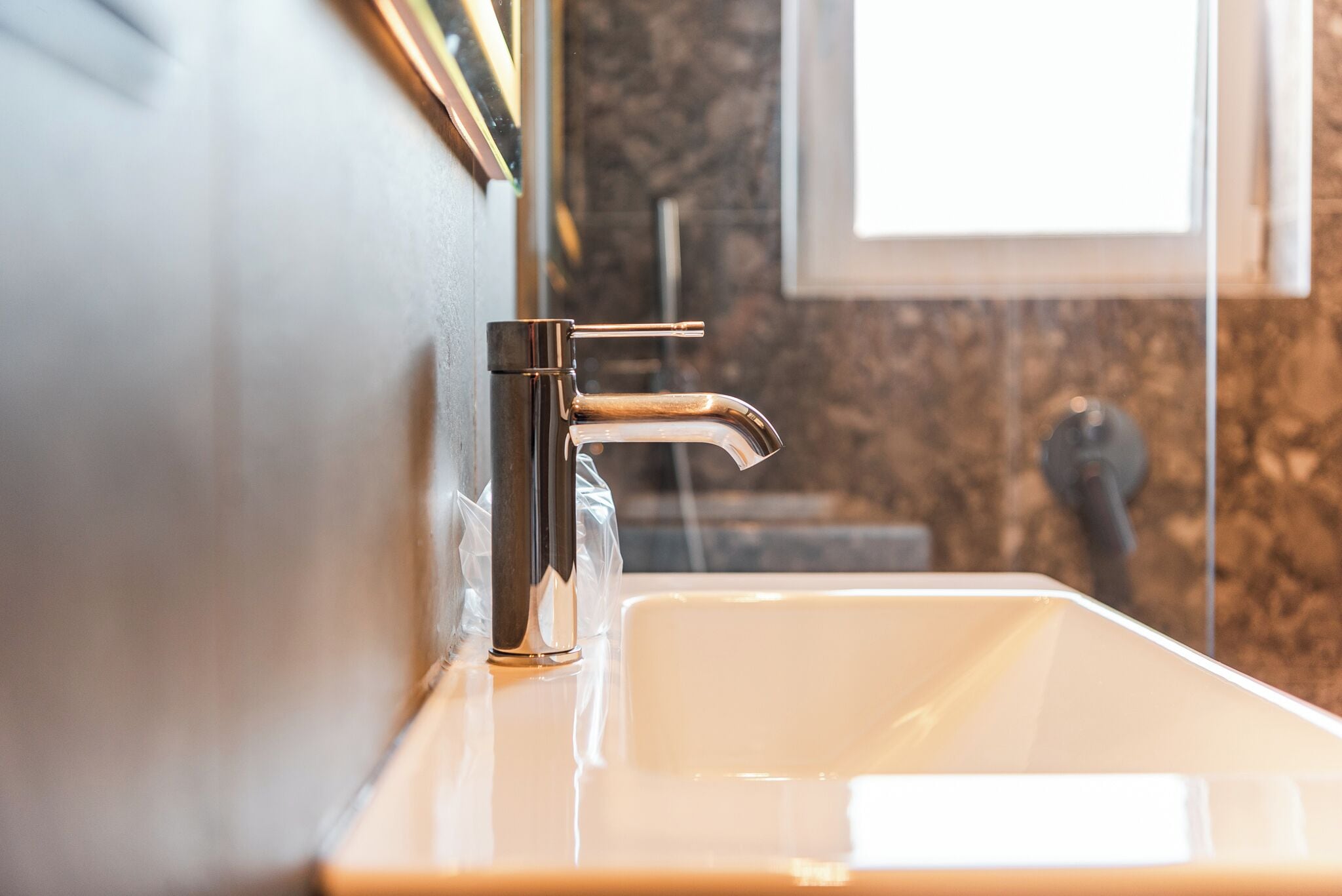 A modern bathroom with a chrome faucet, a white sink, and a marble backsplash.