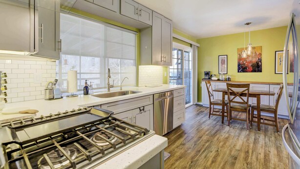 Una cocina moderna con electrodomésticos de acero inoxidable, lavavajillas y un comedor con sillas y mesa de madera.
