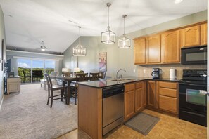 A kitchen with wooden cabinets, stainless steel appliances, and a large island with a dishwasher. - Majestic Sunset Duo: Stay for 14! (Branson)