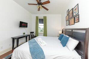 A neatly made bed with a blue throw blanket, a flat-screen TV mounted on the wall, and a ceiling fan. - Modern King bed Haven/Free parking, Pool, Balcony (Santa Rosa Beach)