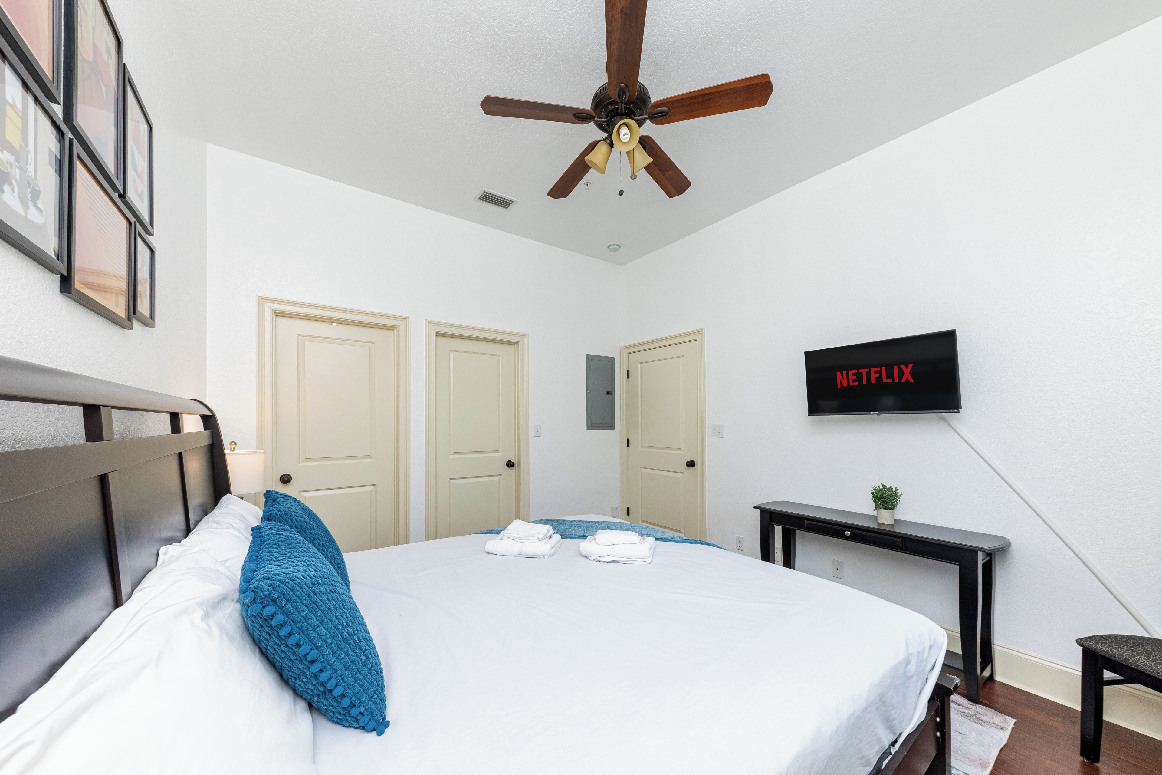 A hotel room with a bed, a ceiling fan, a TV mounted on the wall, and a desk with a plant.