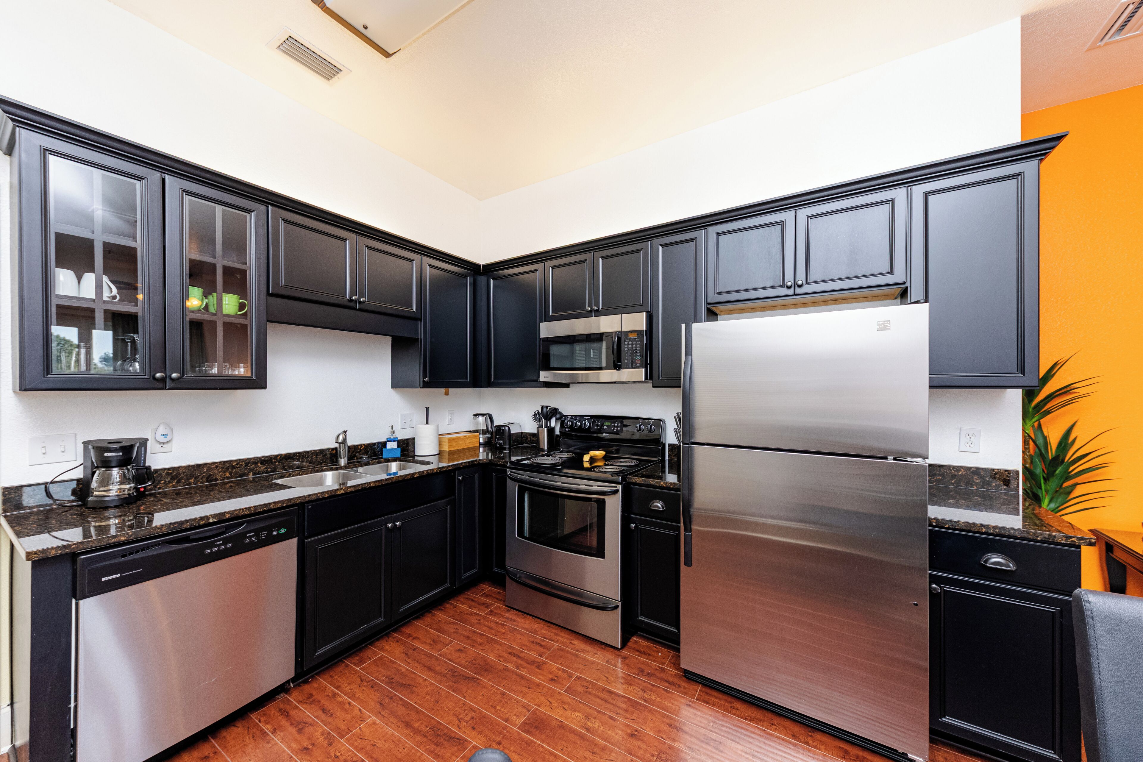 A modern kitchen with black cabinets, stainless steel appliances, and a wooden floor.