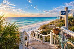 A wooden staircase leading to a beach with a clear view of the ocean, a sign with the number '30A', and a bicycle with a basket.
