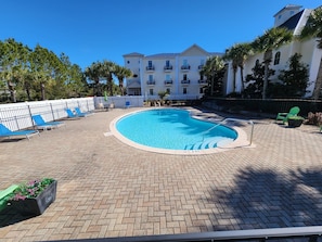A swimming pool with a brick deck, surrounded by lounge chairs and a fence.