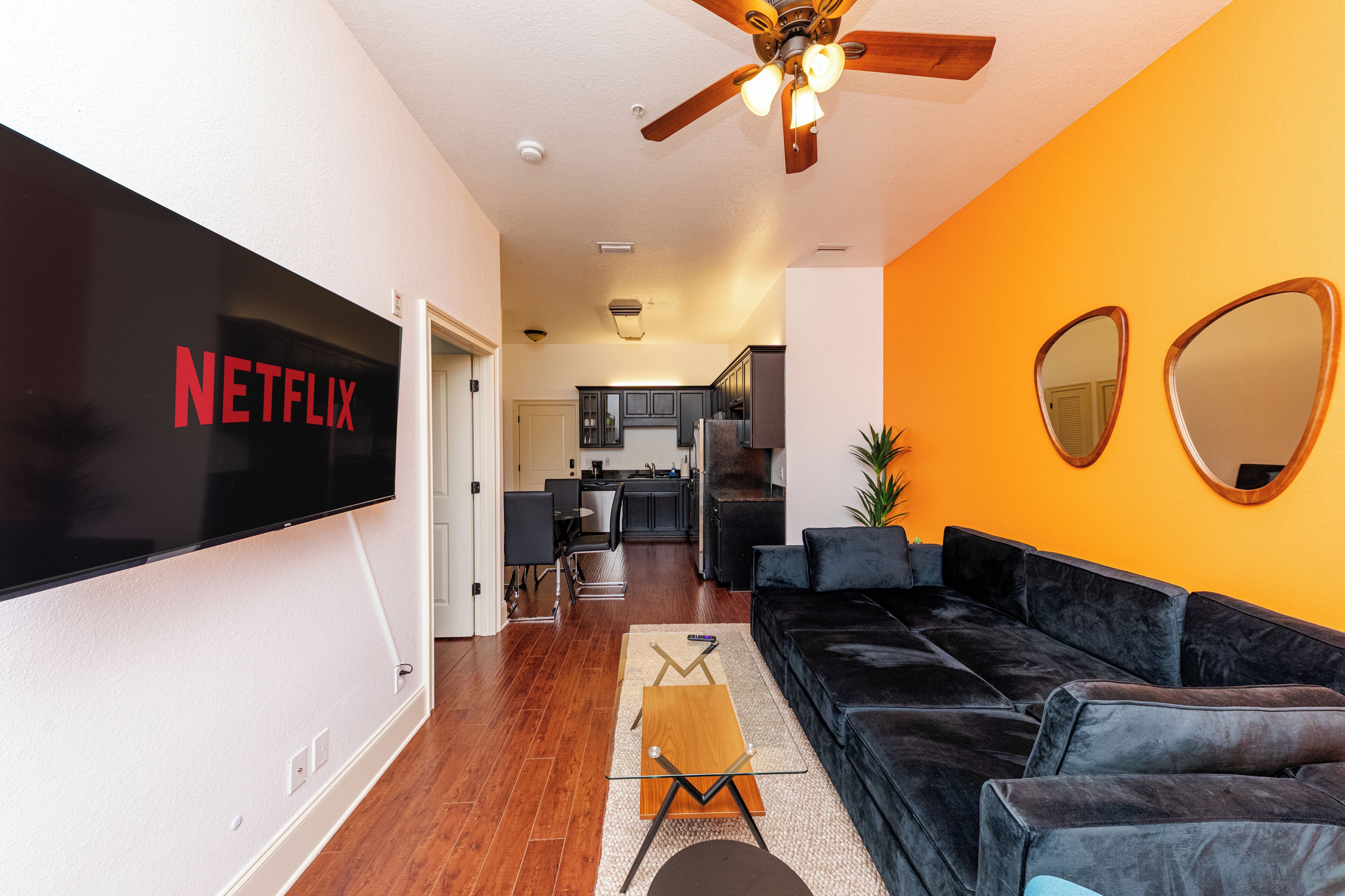 Een woonkamer met een zwarte leren bank, een flatscreen televisie en een plafondventilator.