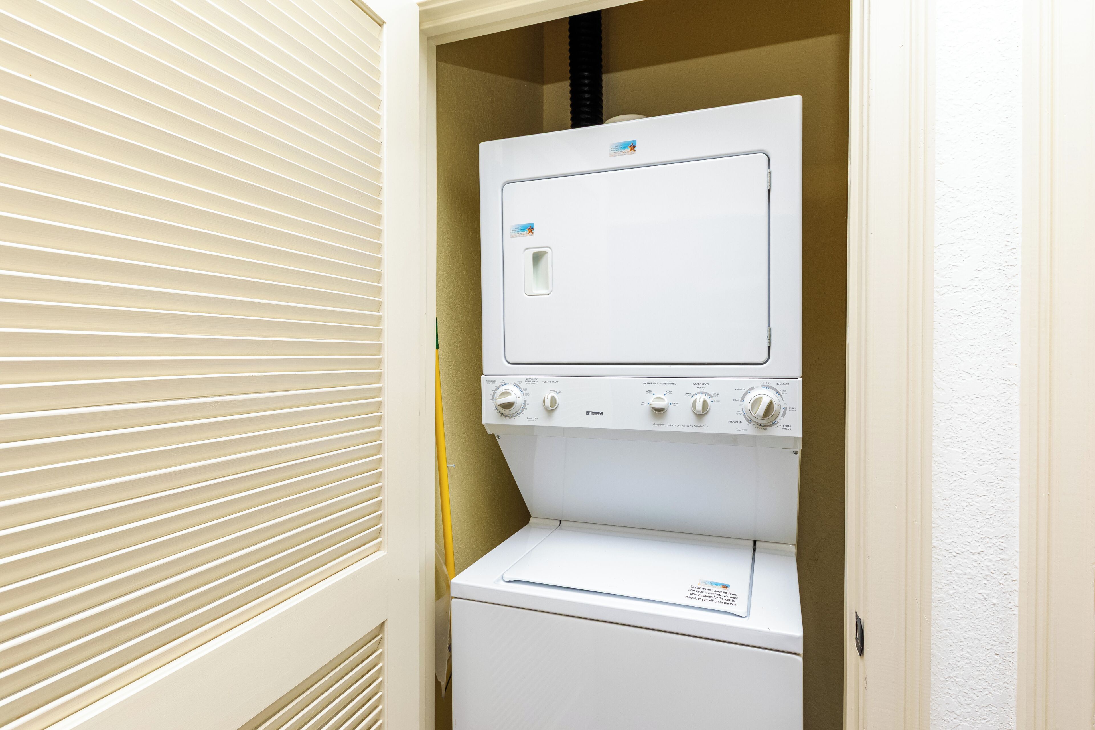 A compact laundry room with a front-loading washer and dryer, a small window, and a door with blinds.