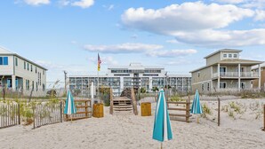 Un hôtel situé en bord de mer, avec une plage de sable, des clôtures en bois et des parasols bleus.
