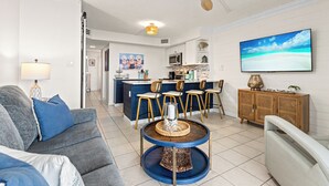 Un salon moderne avec un canapé gris, une table basse ronde et une cuisine en arrière-plan.