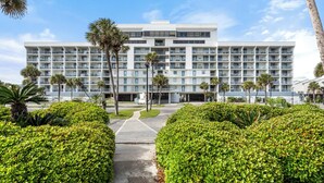 Un hôtel moderne doté de nombreux balcons, entouré d’une végétation luxuriante et bien entretenue ainsi que de palmiers.