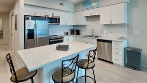 Une cuisine moderne avec des meubles blancs, des appareils en acier inoxydable et un îlot central doté de tabourets de bar.