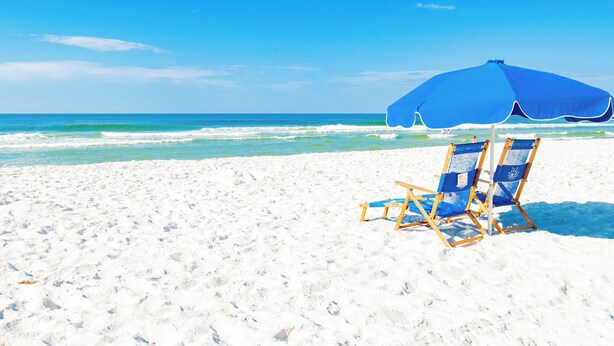 Une plage de sable blanc, un parasol bleu et deux chaises de plage bleues.