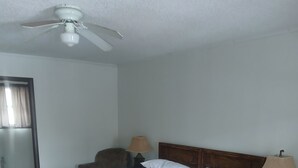 Een hotelkamer met een bed, houten vloer, plafondventilator en nachtkastje met lamp.