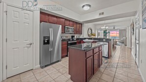 A modern kitchen with stainless steel appliances, wooden cabinets, and a central island. - Legacy Tower II 305 | Stunning Coastal Views! (Gulfport)