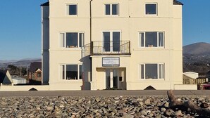 Un edificio de dos pisos con un balcón, un cartel que indica que es un hotel, y un primer plano rocoso.