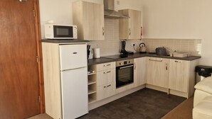 Una cocina compacta equipada con microondas, refrigerador, horno y pileta. En la zona de estar contigua, hay un sofá color crema.