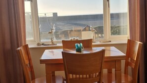 Una habitación con una mesa y sillas de madera, un ventanal con vista al mar y una cortina a la izquierda.