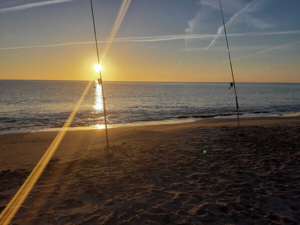A beach with a clear view of the ocean and the sun setting in the distance.