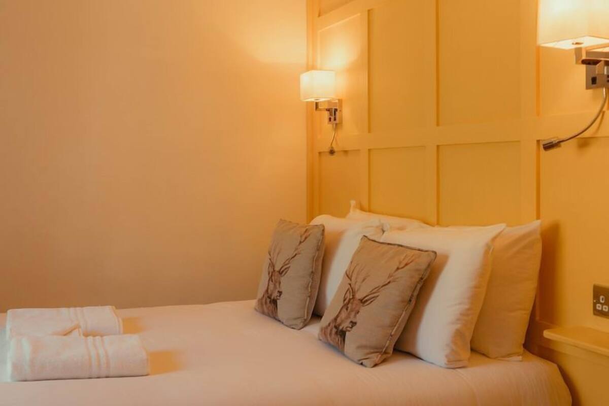 A hotel room with a bed, two wall-mounted lamps, and a neatly made bed with pillows and a folded towel.