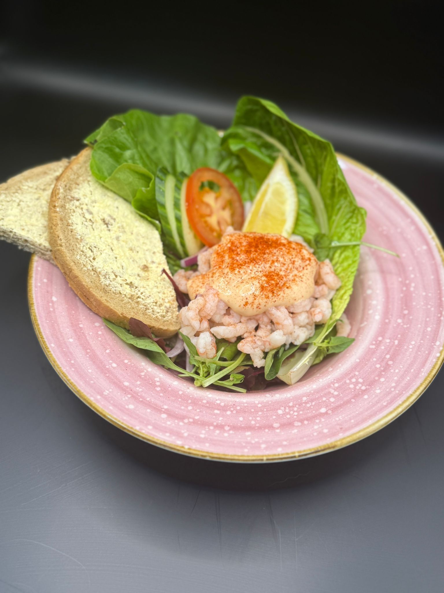 Une assiette contenant une salade de fruits de mer, une tranche de pain, une tomate et un quartier de citron.